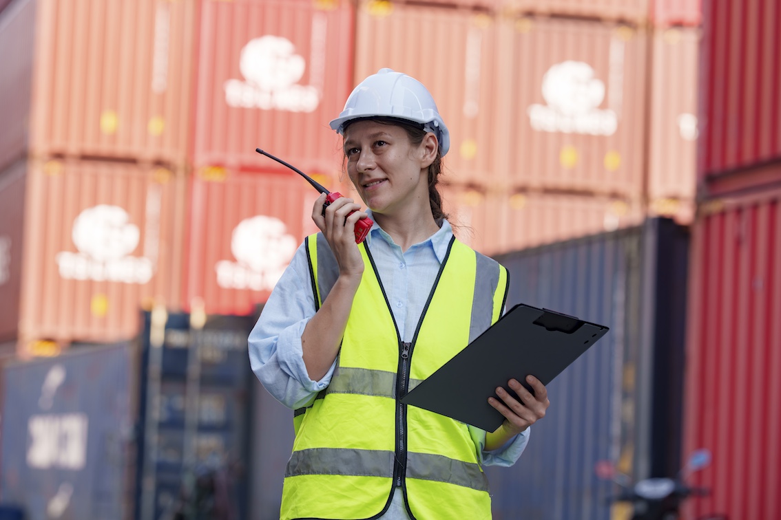 Woman coordinating logistics in a busy shipping yard during daylight hours